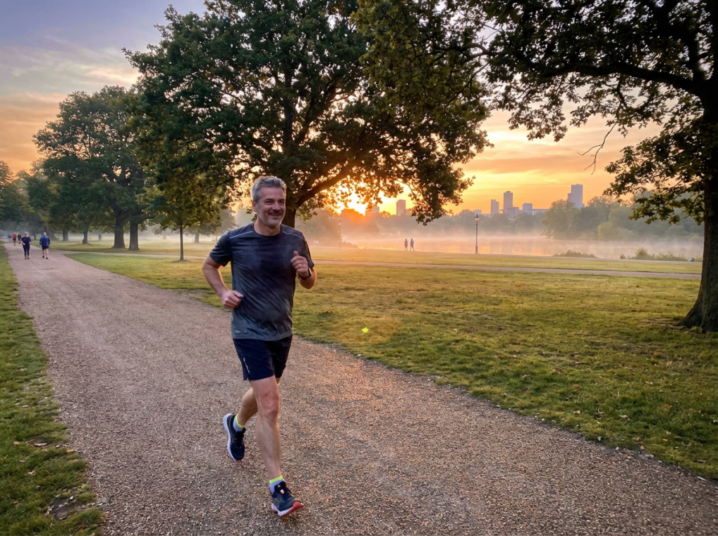 A man jogging on a gravel path in a park during a golden sunrise.
